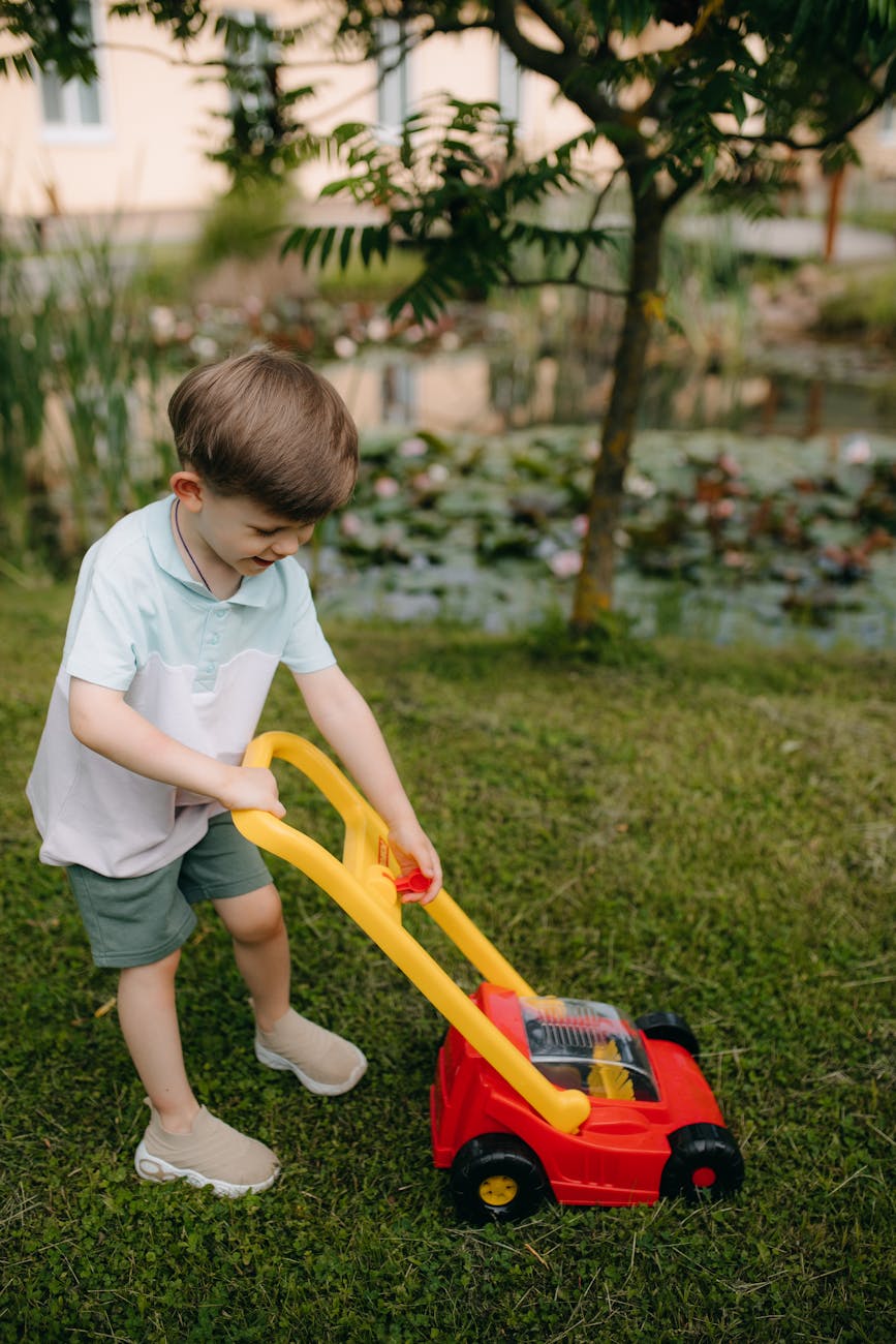 Young boy with toy lawn mower learning about yard work in a sunny garden